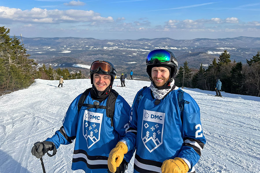 Two men pose on a ski slope wearing blue jerseys