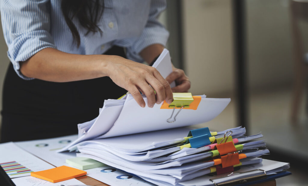 An image of a woman's hands sorting through a stack of files held together with metal clips.